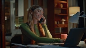 Smiling freelancer calling at night home closeup. Attractive relaxed woman sharing news talking smartphone at dark remote workplace. Happy businesswoman looking laptop speaking telephone in apartment - Powered by Shutterstock - Get 15% off with code: PIKWIZARD15
