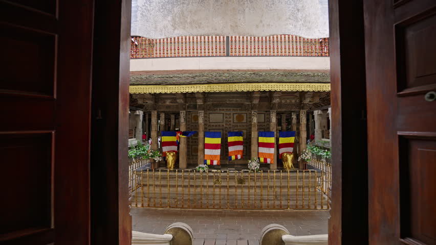 Interior view of Sri Dalada Maligawa, showcasing intricate temple designs, murals, Buddhist flags. Visitors explore sacred site in Kandy, observing religious art, architecture in spiritual sanctuary.