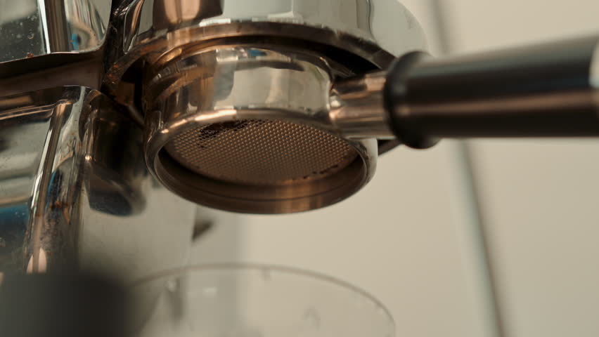 4K Pouring coffee stream from professional machine in cup. Barista man making double espresso, using filter holder. Flowing fresh ground coffee. Drinking roasted black coffee in the morning.