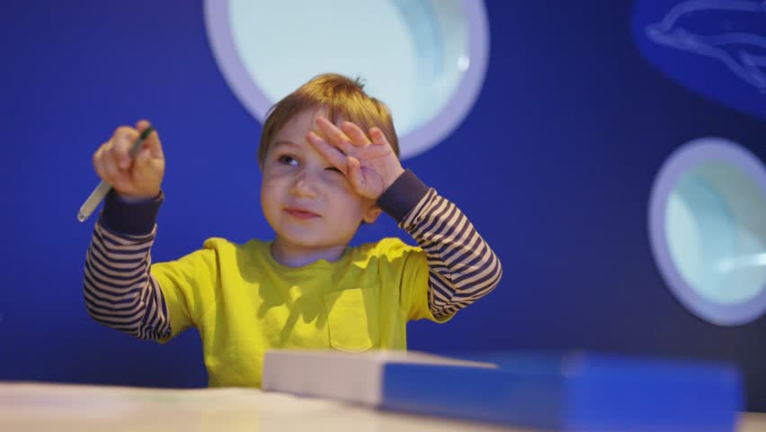 A young boy is sitting at a table with a pen and paper, writing
