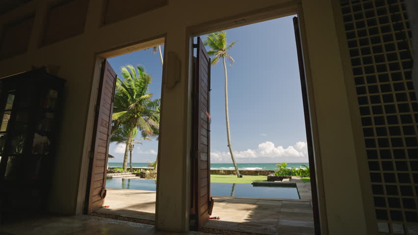 Retro villa living room exit to backyard with swimming pool and ocean shore, horizon, blue sky, palm trees view. Luxury resort patio with blue water pond, sun loungers on hot tropical island day.