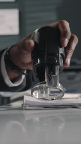 Vertical side closeup of anonymous male lawyer setting his hand and seal on legal document at law firm