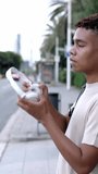 Vertcical HD video of young teenager boy putting headphones to listen music while walking on city street. Student people and technology concept.