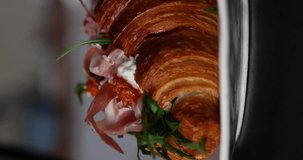 Croissant with ham, cream cheese and arugula on the plate. Vertical video. Beautiful food.