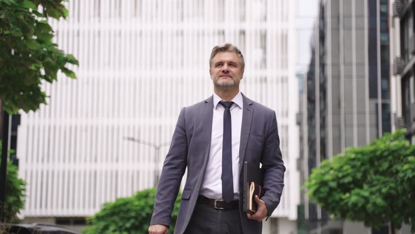 Adult businessman holding laptop and standing on the street. Slow motion