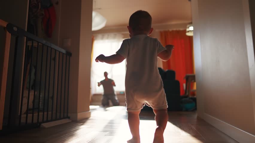 baby toddler first steps. baby son takes first steps around the room to his father sitting by the window glare of the sun learns to walk. happy family kid concept. toddler first dream steps