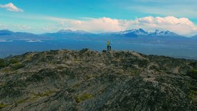 A couple tourist stand on mountain peak overlooking the Beagle Channel at windy day in Ushuaia, Tierra del Fuego, Argentina. Aerial drone video.