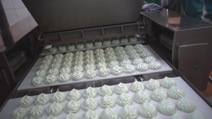 Conveyor belt moving white cupcakes in bakery kitchen
