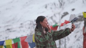 Portrait of Indian girl holding smart phone while standing against mountains and talking in video call at Lahaul, Himachal Pradesh, India. Tourist talking with family. Indian woman videocall.