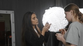 Model and production team in the studio. Model and assistant fixing makeup and talking, photographer sets up studio lightning. - Powered by Shutterstock - Get 15% off with code: PIKWIZARD15