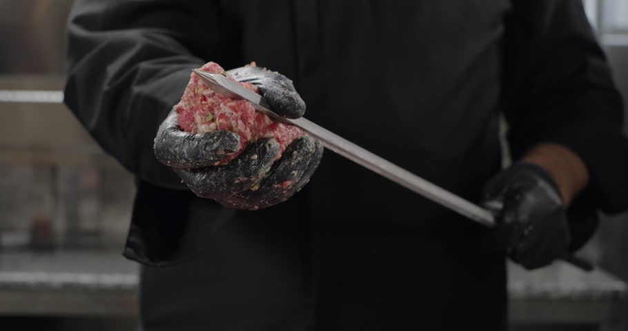 Chef prepares kebab, shapes Turkish Adana kebab, spreads ground meat along the skewer using hands. Close-up