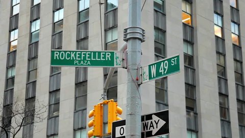 New York City shot of two street signs on the corner of Rockefeller Plaza and W 49 Th Street. A small bird lands on the sign before flying away, playing with another one.