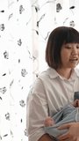 Vertical slow-motion video of a Taiwanese mother in her 20s assing a baby girl who is 1 month old in front of an indoor curtain