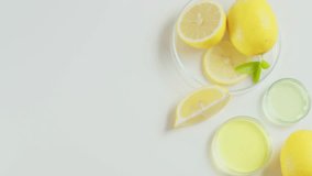Scientist with medical gloves take out and shake gently a petri dish with yellow fluid and a lemon slice soaked in, decorated by a dish of lemon on white table. Top view, blank space