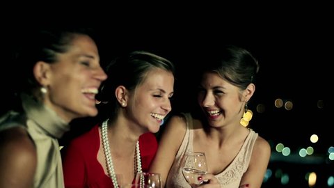 Three female friends enjoying night party on the terrace, crane shot
