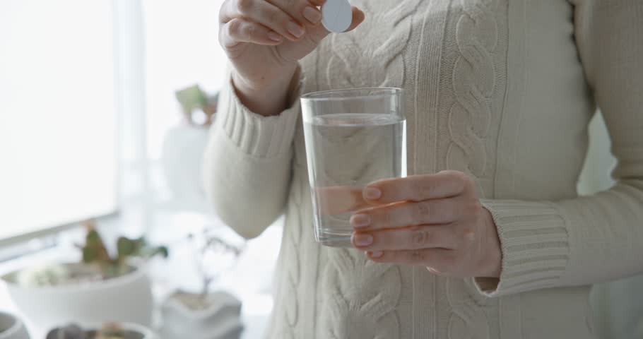 pharmacy and treatment concept - Close-up of woman throwing effervescent tablet in a glass of water