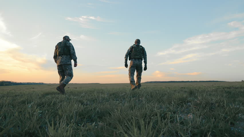 Soldiers Walking Through Open Field at Dusk, Two soldiers in camouflage gear trekking across a field.