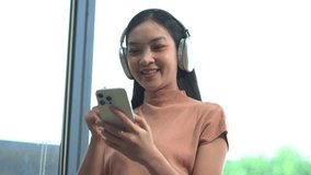 Smiling girl relaxing at home, she is playing music using smartphone tablet, laptop, and wearing white headphones.