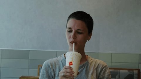 Caucasian woman with short pretty hair cut in fast food restaurant McDonalds drinking cold drink using paper disposable cup and enjoys. Belgrade, Serbia- 04.28.2024 Redaksjonell arkivvideo