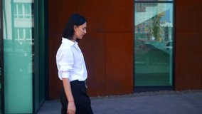 Business Woman looking at her watch near the business center. Office worker, vacation, director, formal attire. Happy Lady in white shirt and black pants. Business smiling entrepreneur. Successful Wom