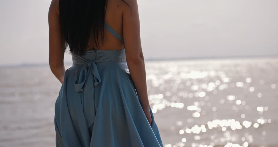 Woman holding blue dress at the sea, back view, slow motion