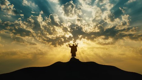 Silhouette of Jesus praying on hill crest with sun rays and mystic clouds behind Him. Extreme Long Shot
