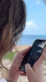 A girl is taking picture with her smartphone on a beach Young brunette woman makes video on the beach, selective focus. High quality 4k footage