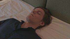 Young man lying dressed in clothes on a bed unconscious or sleeping exhausted. Stock clip. Caucasian male lying on bed in a room with eyes closed.