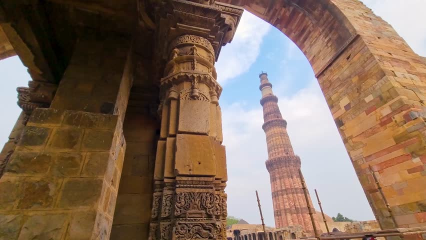 panning reveal shot showing the famous landmark monument Qutub minar from an arch in the complex this is a heritage monument in India and a popular tourist destination