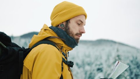Beautiful mountains in winter time. Man with beard, wearing yellow winter clothes goes with a tourist map in hands, goes along the mountain road against the background of the winter landscape – Video có sẵn