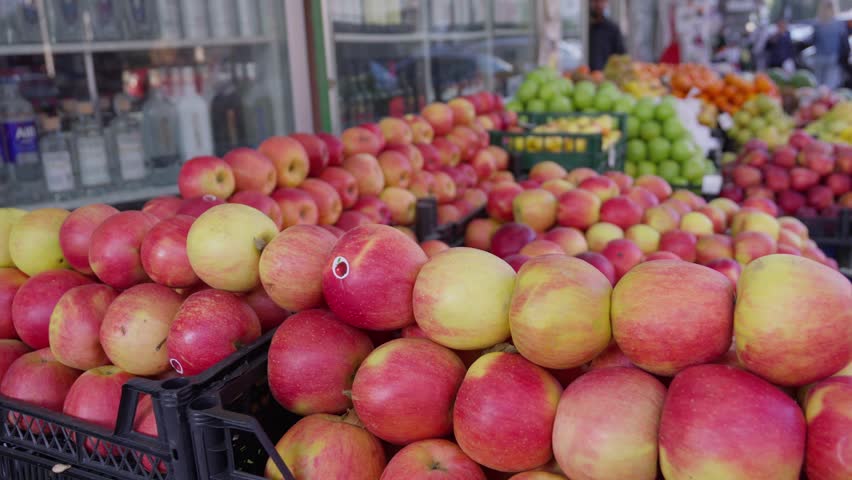 Apples and other fruits stacked on shelves of different colors in row at street market in city of Batumi. Street trade. Case. Close-up of fresh apples on fruit display.