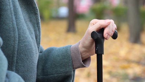 Elder woman has pain in her hands trembling and leaning on walking stick outside