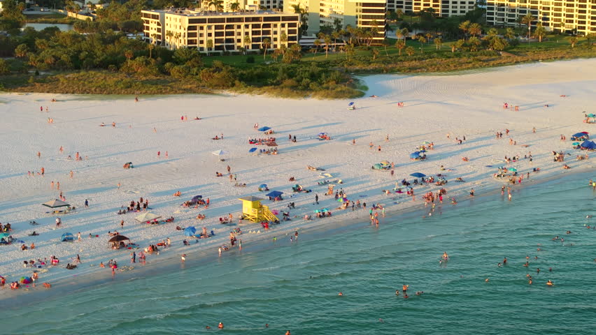 Siesta Key beach in Sarasota, USA. Many people enjoying vacation time swimming in gulf water and relaxing on warm Florida sun at sunset