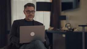 Mature male professional focusing on work using laptop in hotel room. Businessman working at home with computer, thinking. Mid adult man looking busy. Entrepreneur managing business online. - Powered by Shutterstock - Get 15% off with code: PIKWIZARD15