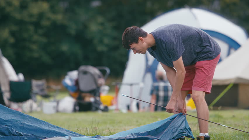 Young man unpacking and setting up tent for camping at outdoor summer music festival - shot in slow motion