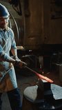Blacksmith in apron, safety glasses and protective gloves forging hot metal workpiece with hydraulic press machine when working in foundry. Vertical clip