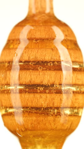 Thick organic honey dripping from a wooden honey spoon, isolated on white background