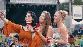 Three female friends wearing glitter and holding drinks posing for selfie at outdoor summer music festival - shot in slow motion - Powered by Shutterstock - Get 15% off with code: PIKWIZARD15