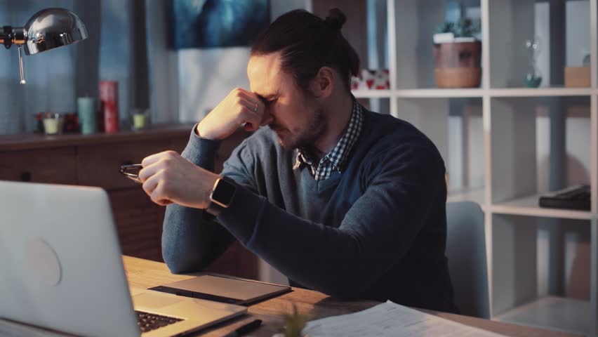 Sleepy young guy sitting in front of the computer in the modern office late at night decides to have a rest, rubs his eyes, checks the time, puts his head on working desk. Workaholic | Shutterstock HD Video #34954927