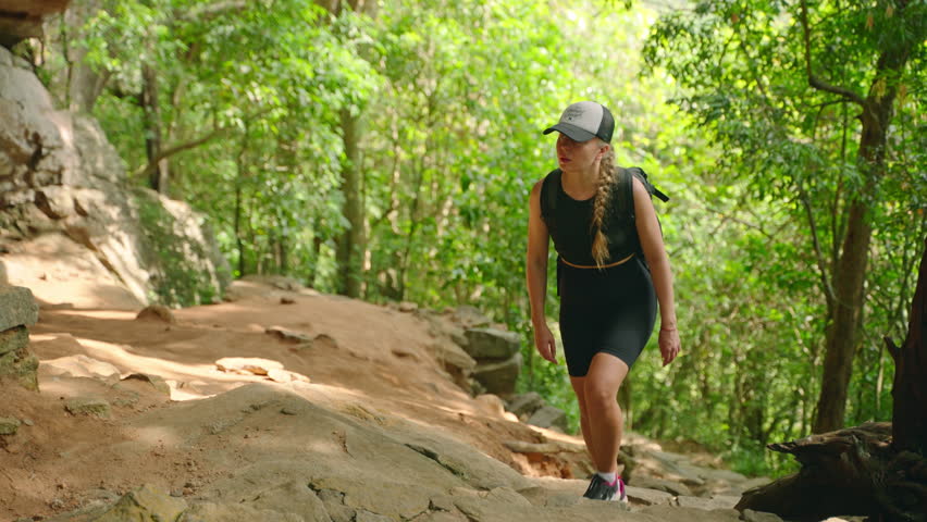 Active woman in sportswear hikes through rugged mountain terrain, exploring natural grotto. Adventure travel scene with female trekker ascending steep rocky path, immersed in wilderness area. Slowmo