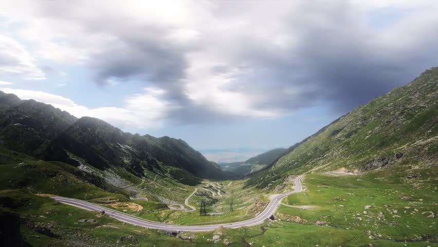 Road surrounded by mountain with stormy time-lapse clouds