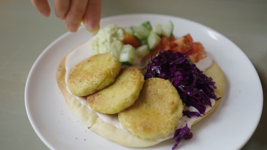 Women's hands squeeze lemon juice onto fresh falafel cutlets on a pit with vegetables and hummus, a delicious and healthy Vagan dish.