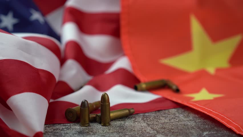 Hand of unrecognizable person placing a large caliber bullet in the middle of an American and Chinese flag. 