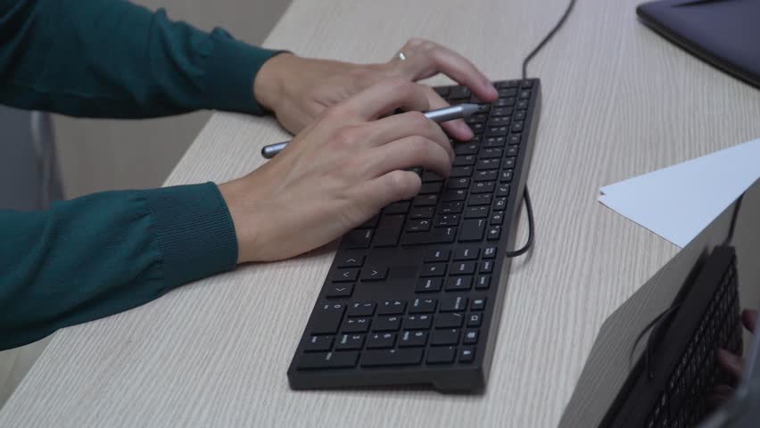 Side view of an unrecognizable man working in the office, using a computer keyboard and digital tablet, close-up view of the hands
