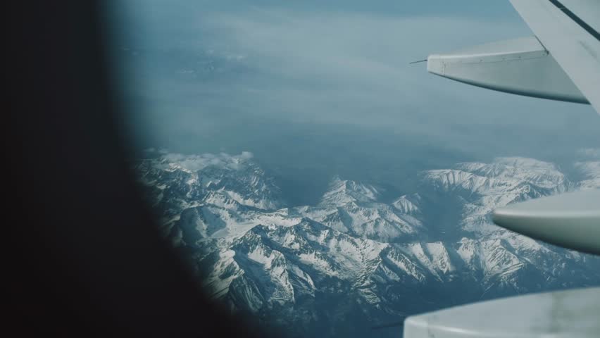 Aerial view of mountains in dawn through plane window. Airplane Window View Above the Clouds. Airplane flight. Wing of an airplane flying above the clouds.