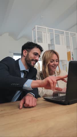 Vertical. Teamwork of businesspeople working and cooperating together on a corporate project. Two startup colleagues talking while using a laptop computer at office workplace. Coworkers partnership