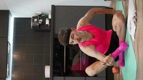 Funny looking man with mustache and pink sports clothes doing workout exercises with bananas and kissing biceps. Vertical video