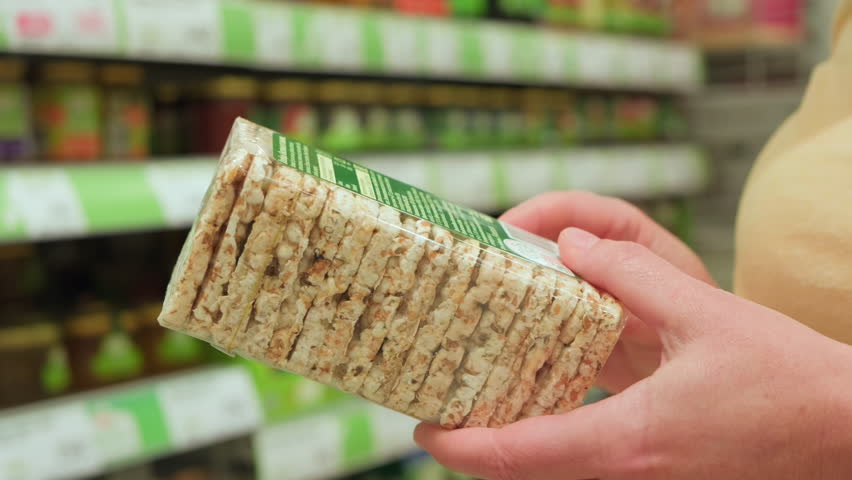 Vegan shopper reading label on bio organic rice crispbread in vegetarian section of supermarket.