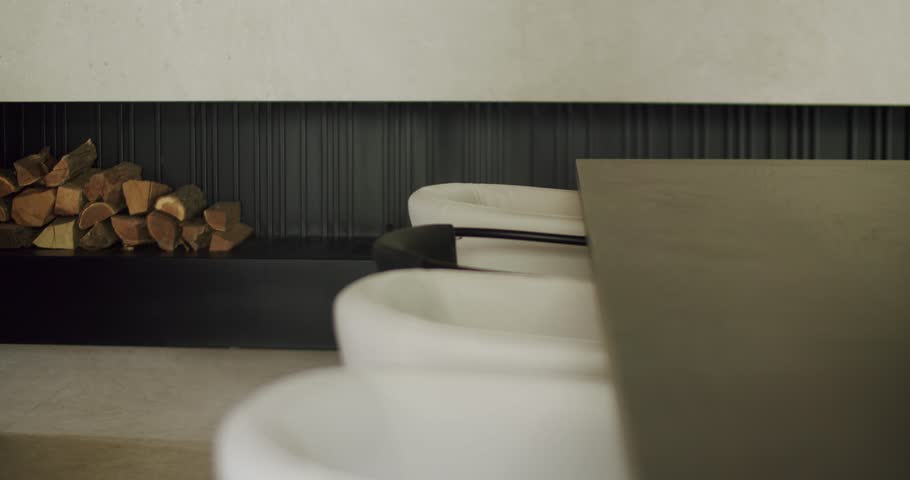 Contemporary living room features a sleek black fireplace, neatly stacked firewood, and elegant white sofas. A person is partially visible, adding a human touch to the minimalist design.