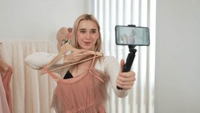 Young social medial content creator woman make fashion video using selfie stick. Blogger smile to camera while making persuasive online clothing sell vlog to audience or follower. Blithe